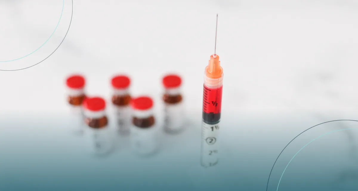 Syringe filled with red liquid beside red-capped medication vials