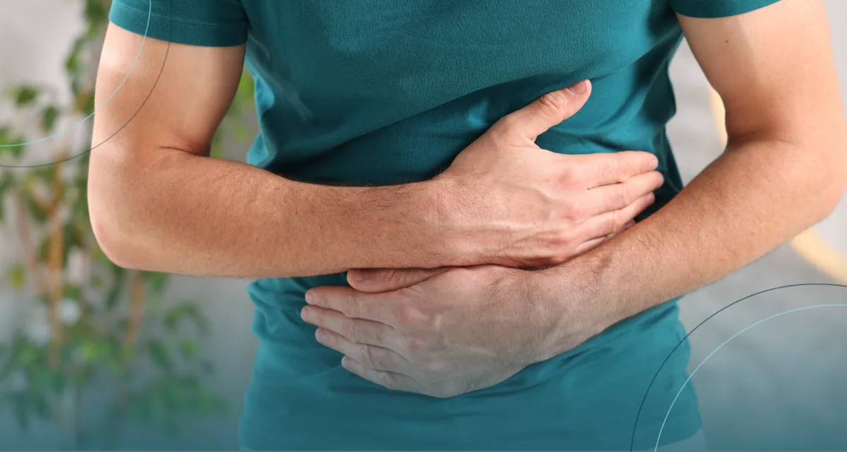 Man in a teal shirt holding his stomach in discomfort
